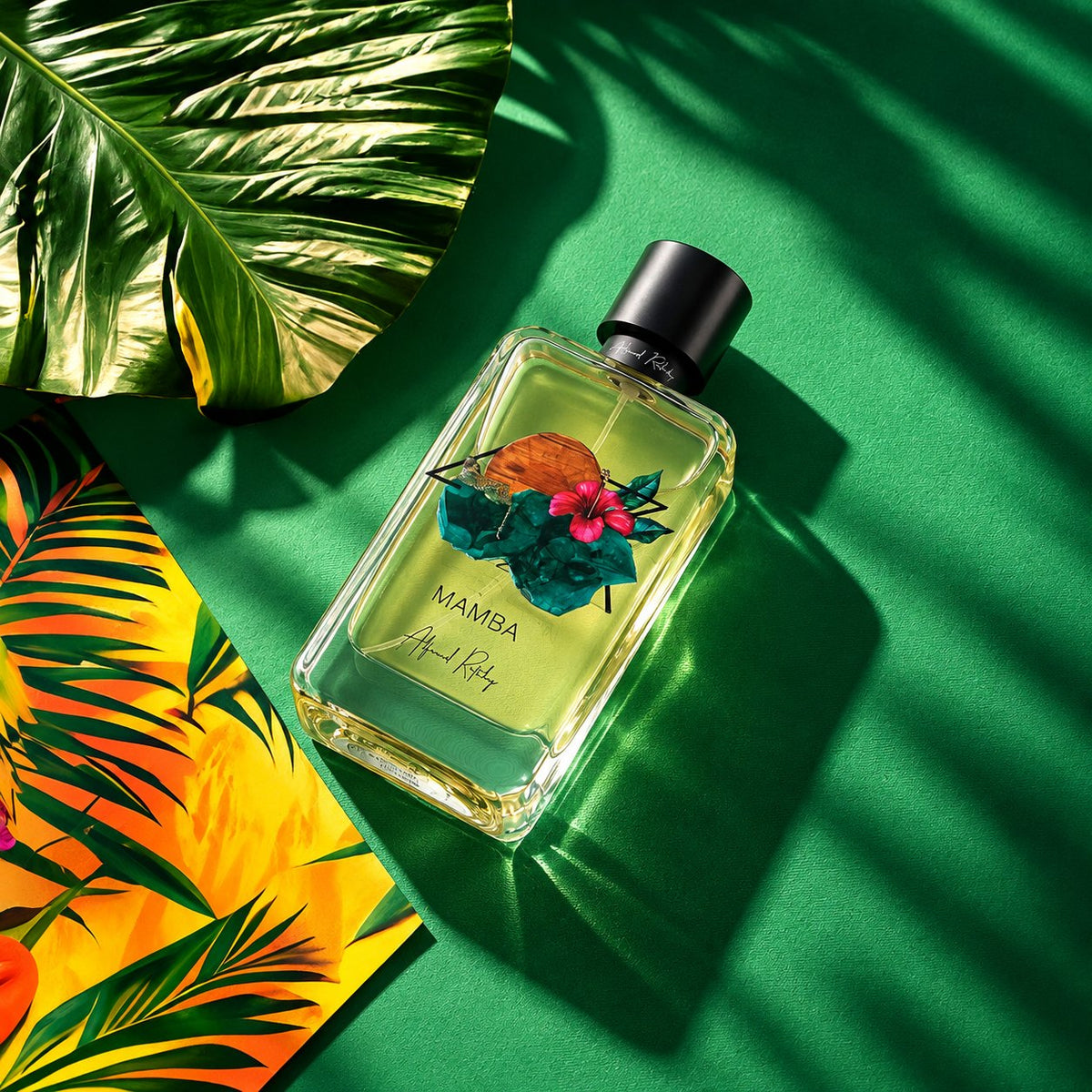 Mamba d'Alfred Ritchy, eau de parfum 100 ml, flacon posé à plat sur fond vert, entre des feuilles de palmier.