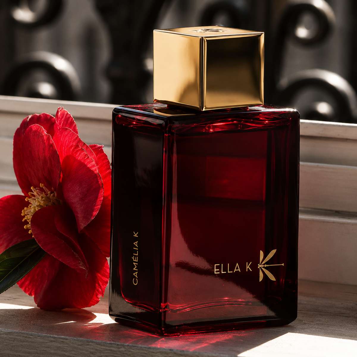 Camélia K d'Ella K, eau de parfum, flacon en mise en scène accompagné d'une fleur de camélia rouge.