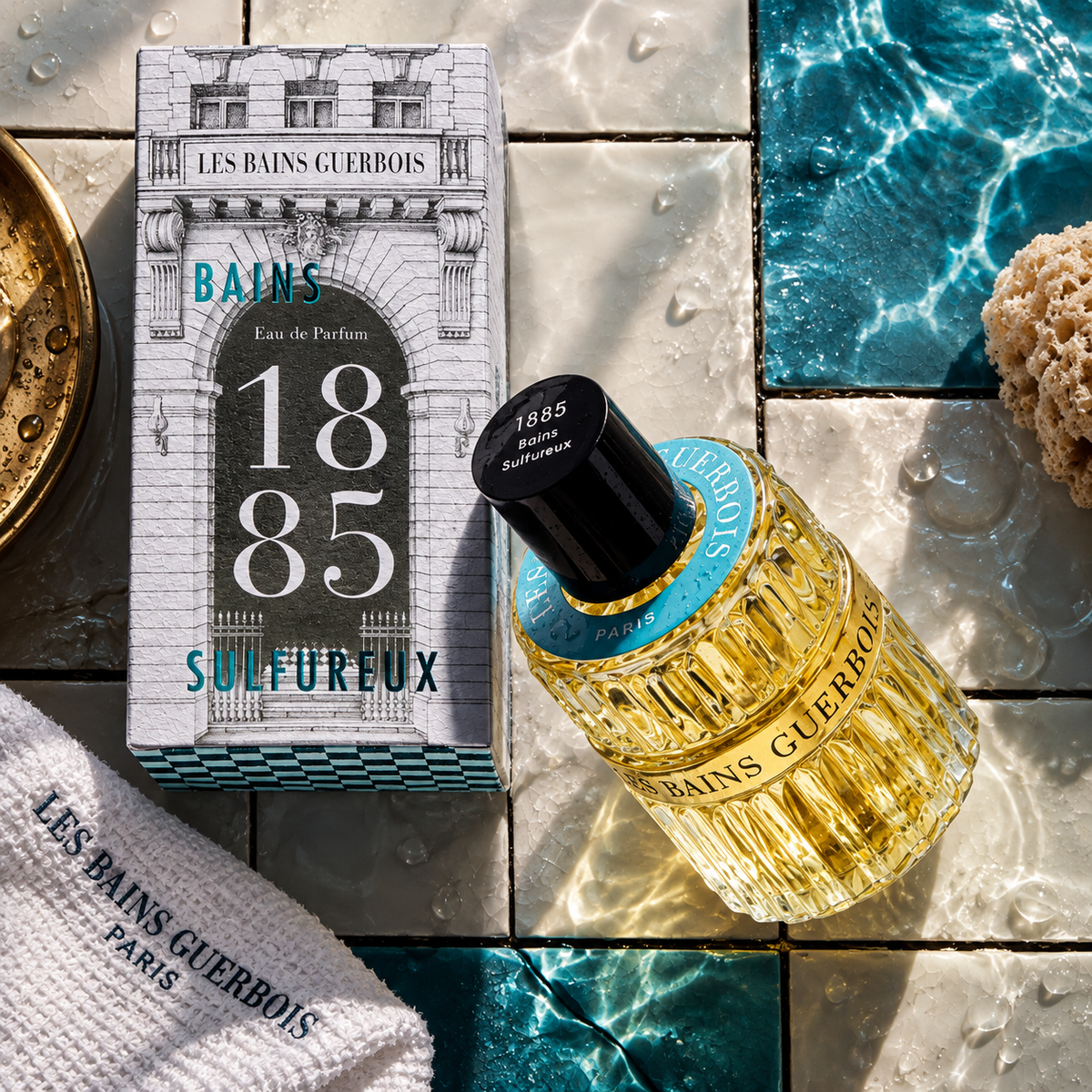 1885 Bains Sulfureux de Les Bains Guerbois, eau de parfum 100 ml, flacon et étui sur un carrelage de bain humide au bord de l'eau.