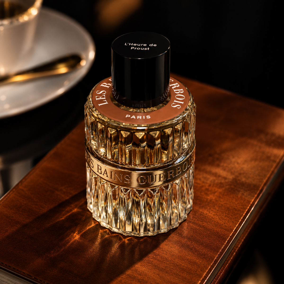 1900 L'Heure de Proust de Les Bains Guerbois, eau de parfum 100 ml, flacon posé sur un cuir brun près d'une tasse de café, dans une lumière chaude.