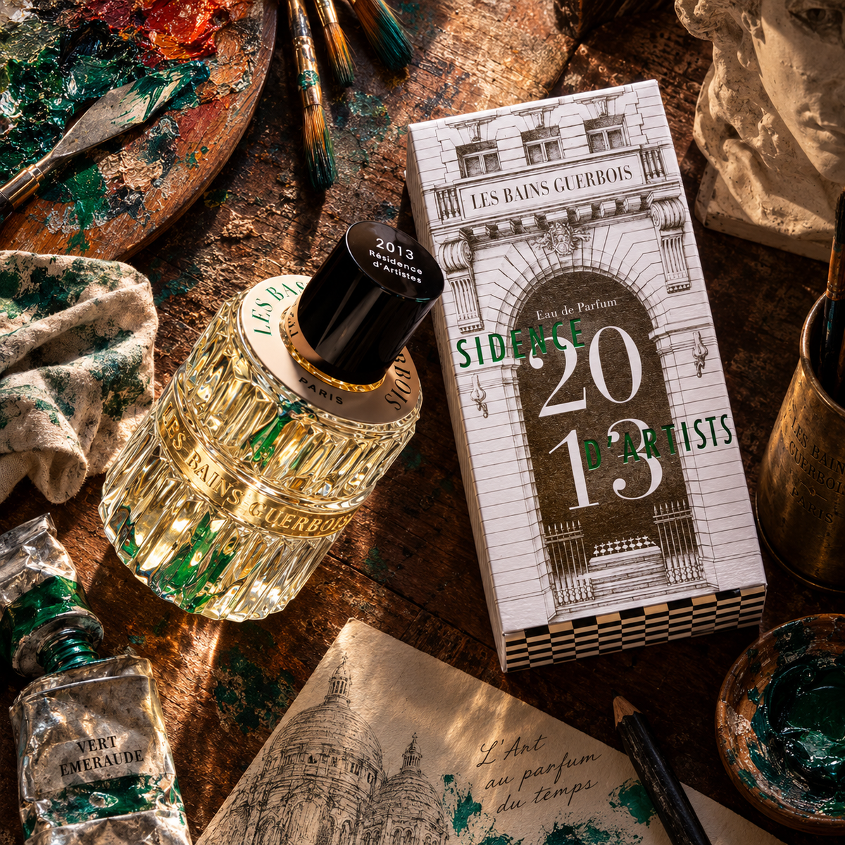 2013 Résidence d'Artistes de Les Bains Guerbois, eau de parfum 100 ml, flacon et étui sur un établi d'atelier de peintre, entre pinceaux et tubes de couleur.