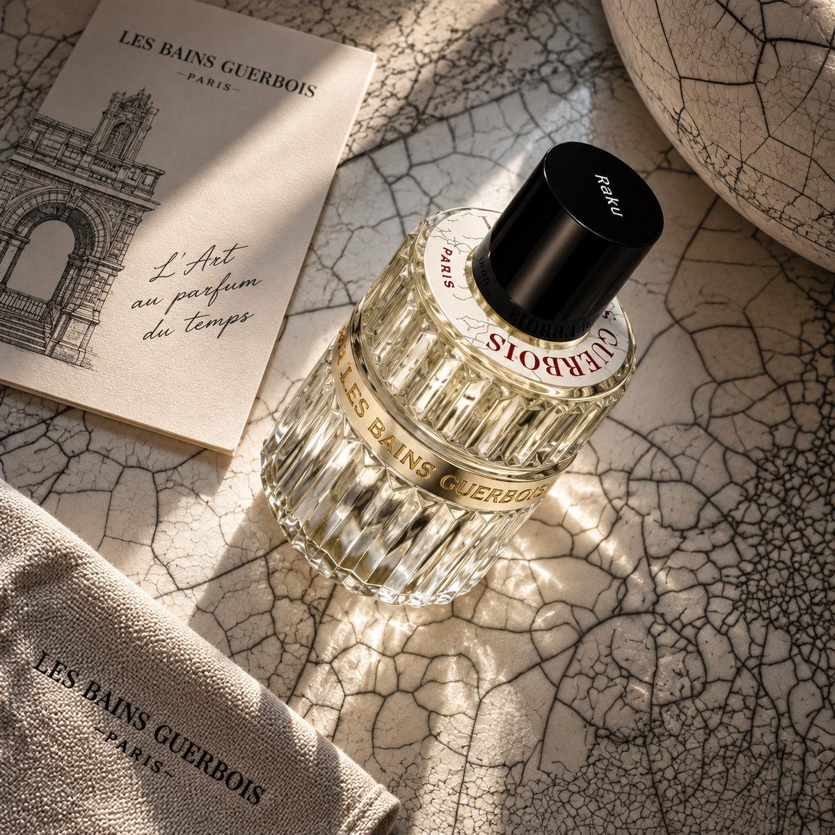 Raku de Les Bains Guerbois, eau de parfum 100 ml, flacon sur une surface de céramique craquelée, à côté d'un pochon de toile.