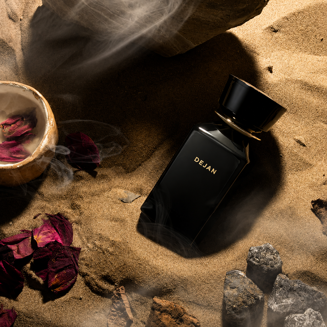 Dejan by Oman Luxury flacon de parfum dans un décor de sable, roses séchées et pierres naturelles