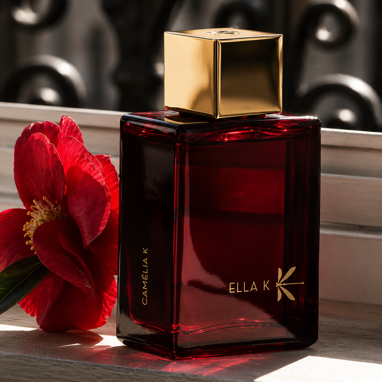 Parfum Camélia K Ella K accompagné d’une fleur de camélia rouge dans une ambiance élégante et lumineuse