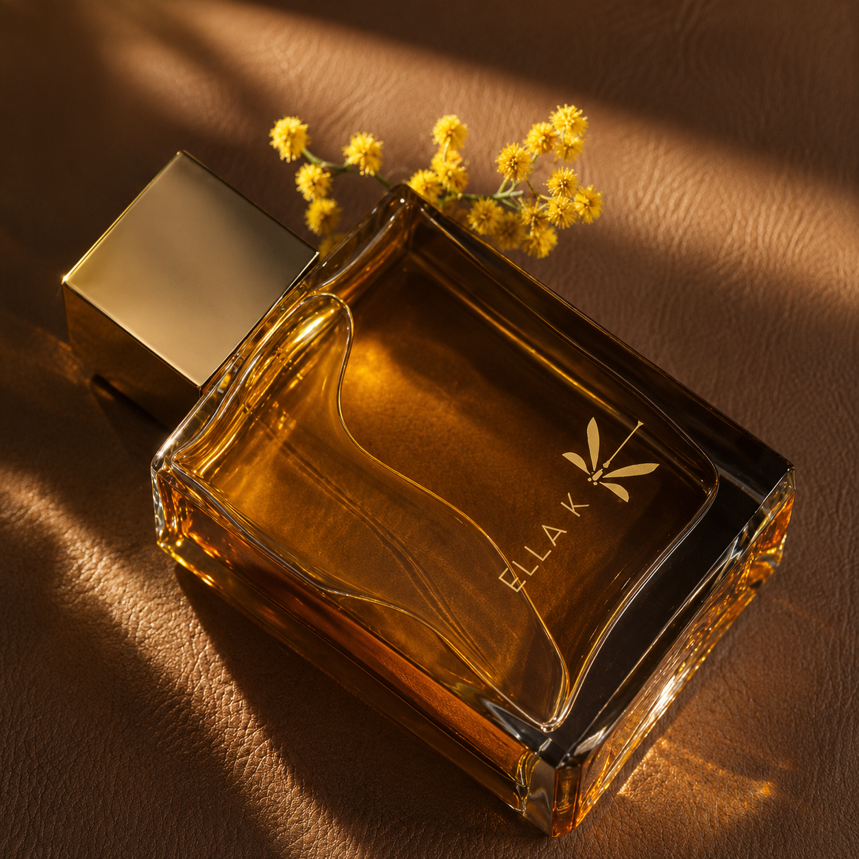 Reflet sur l'Okavango d'Ella K, eau de parfum, flacon en mise en scène sur une surface brune, parmi des fleurs jaunes et une lumière dorée.