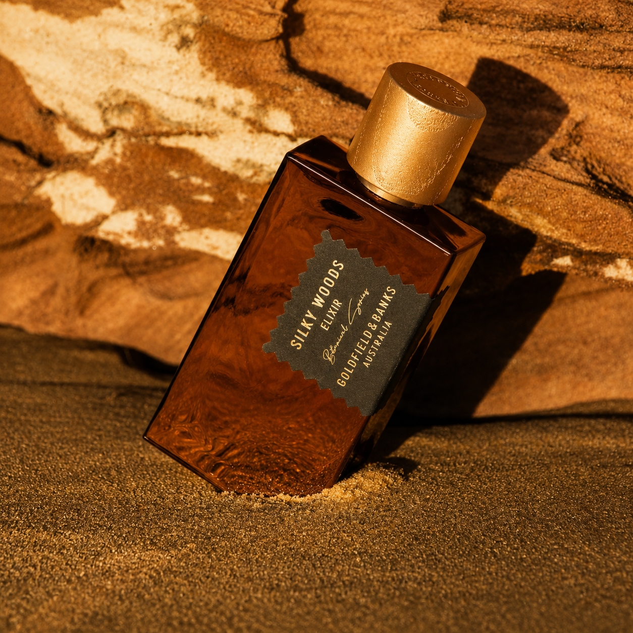 Parfum Silky Woods Elixir Goldfield & Banks Australia en mise en scène sur roche aux tons ambrés et boisés avec lumière dorée