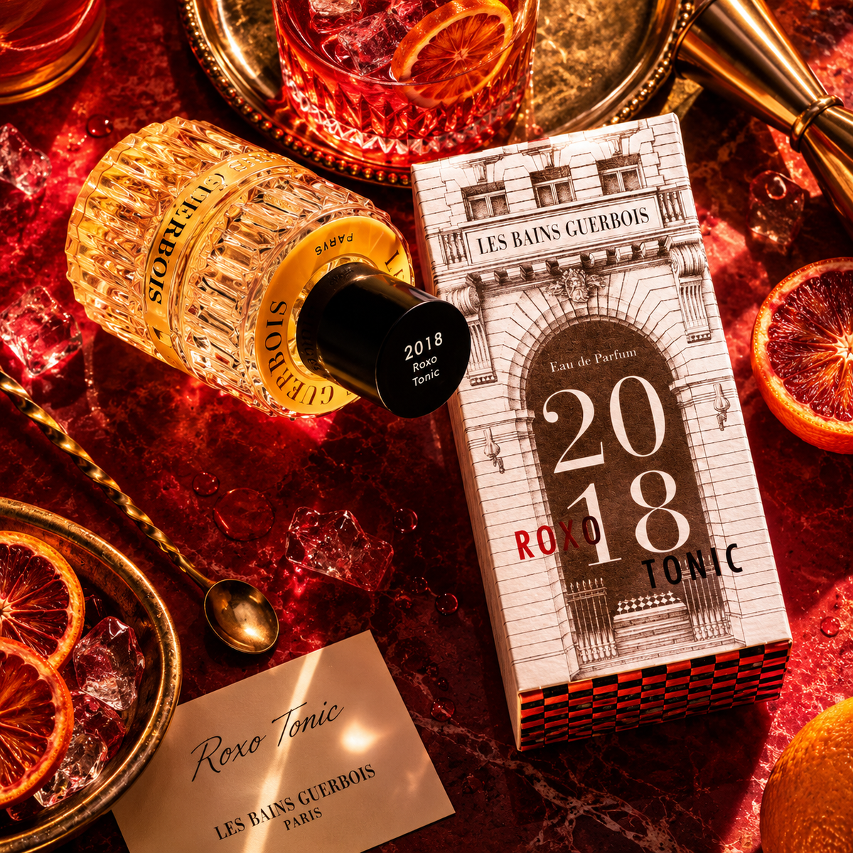 2018 Roxo Tonic de Les Bains Guerbois, eau de parfum, flacon et étui sur un marbre rouge, entre oranges sanguines et glaçons.